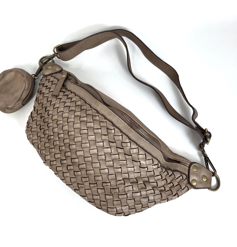 Puede incluir: Ri&ntilde;onera de cuero trenzado en color topo. Cuenta con un compartimento principal con cremallera, un peque&ntilde;o monedero adjunto y una correa ajustable. El dise&ntilde;o trenzado le da una textura &uacute;nica. Un accesorio elegante y pr&aacute;ctico.
