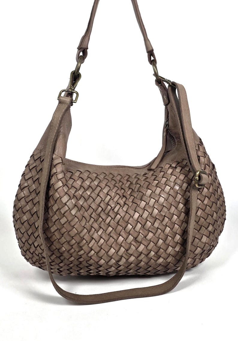 May include: A woven leather shoulder bag in a neutral taupe color. The bag features a large, rounded shape with a woven pattern across the body. It has a long, adjustable strap and a shorter shoulder strap, both in matching leather.