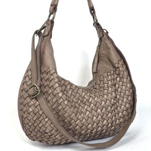 May include: A taupe-colored hobo bag with a woven design on the front. The bag has a single shoulder strap and a smaller adjustable strap. The bag is made of a soft, leather-like material and features brass-colored hardware.