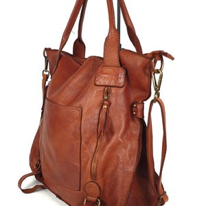May include: A brown leather tote bag with a shoulder strap and a zipper closure. The bag has a front pocket and a detachable shoulder strap. The bag is made of a soft, textured leather.