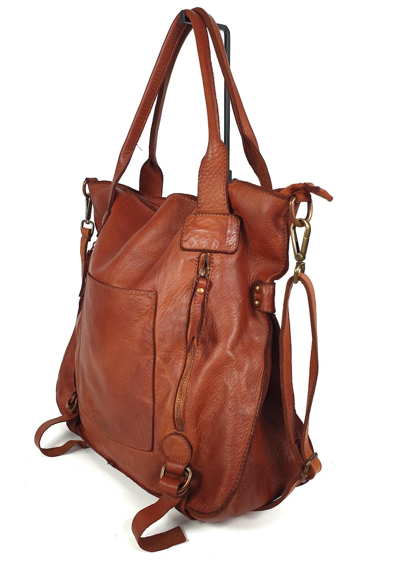 May include: A brown leather tote bag with a shoulder strap and a zipper closure. The bag has a front pocket and a detachable shoulder strap. The bag is made of a soft, textured leather.