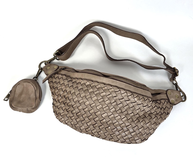 Puede incluir: Un bolso de cintura de cuero tejido de color topo con un peque&ntilde;o monedero a juego. El bolso tiene una correa larga ajustable y dos compartimentos con cremallera. El monedero tiene cierre de cremallera. Los herrajes son de metal oscuro.