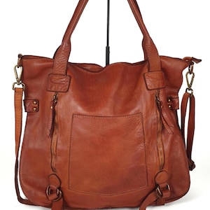 May include: A brown leather tote bag with two top handles and a detachable shoulder strap. The bag has a front pocket, two zippered compartments, and metal hardware. The leather has a distressed look.
