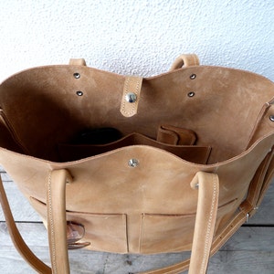 Puede incluir: Un bolso tote de cuero marr&oacute;n claro con dos bolsillos grandes en la parte delantera y dos bolsillos m&aacute;s peque&ntilde;os en los laterales. El bolso tiene una cremallera y dos asas superiores.