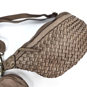 Puede incluir: Ri&ntilde;onera de cuero tejido en color topo neutro. La bolsa tiene un compartimento principal con cremallera y un monedero m&aacute;s peque&ntilde;o adjunto. La correa es ajustable y los herrajes son de color lat&oacute;n. La bolsa est&aacute; dise&ntilde;ada con un patr&oacute;n de tejido de cesta.