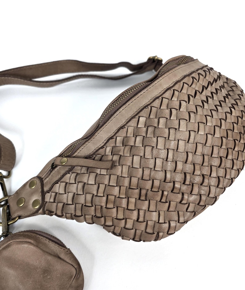 Puede incluir: Ri&ntilde;onera de cuero tejido en color topo neutro. La bolsa tiene un compartimento principal con cremallera y un monedero m&aacute;s peque&ntilde;o adjunto. La correa es ajustable y los herrajes son de color lat&oacute;n. La bolsa est&aacute; dise&ntilde;ada con un patr&oacute;n de tejido de cesta.