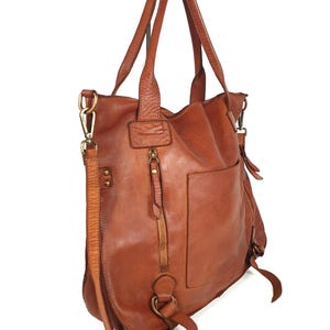 May include: A brown leather tote bag with a shoulder strap and a top handle. The bag has a front pocket, a zipper closure, and metal hardware. The leather has a distressed look.