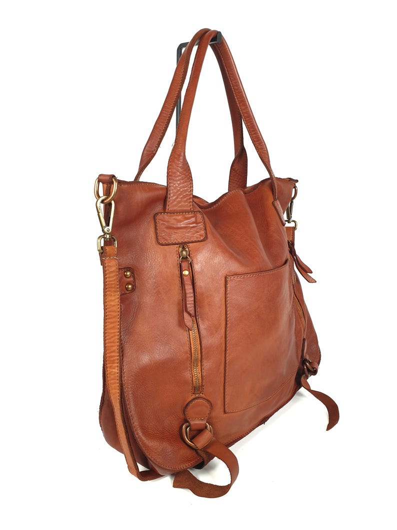 May include: A brown leather tote bag with a shoulder strap and a top handle. The bag has a front pocket, a zipper closure, and metal hardware. The leather has a distressed look.