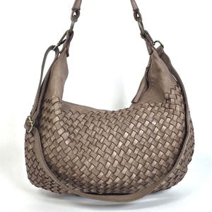 May include: A taupe-colored shoulder bag with a woven design. The bag features a single shoulder strap and an adjustable crossbody strap. The bag is made of leather and has a soft, slouchy shape. The bag is suitable for everyday use.