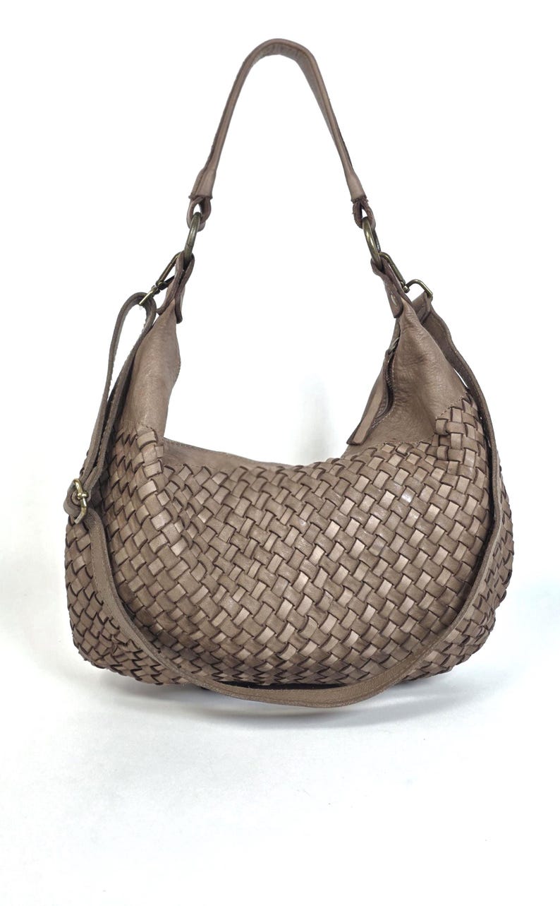 May include: A taupe-colored shoulder bag with a woven design. The bag features a single shoulder strap and an adjustable crossbody strap. The bag is made of leather and has a soft, slouchy shape. The bag is suitable for everyday use.