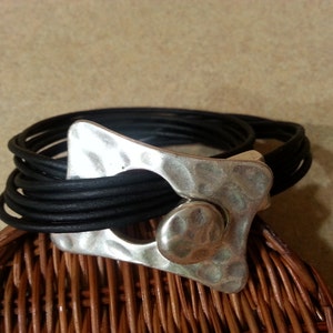 May include: A black leather wrap bracelet with a hammered silver clasp. The clasp has a large, round, hammered silver accent.