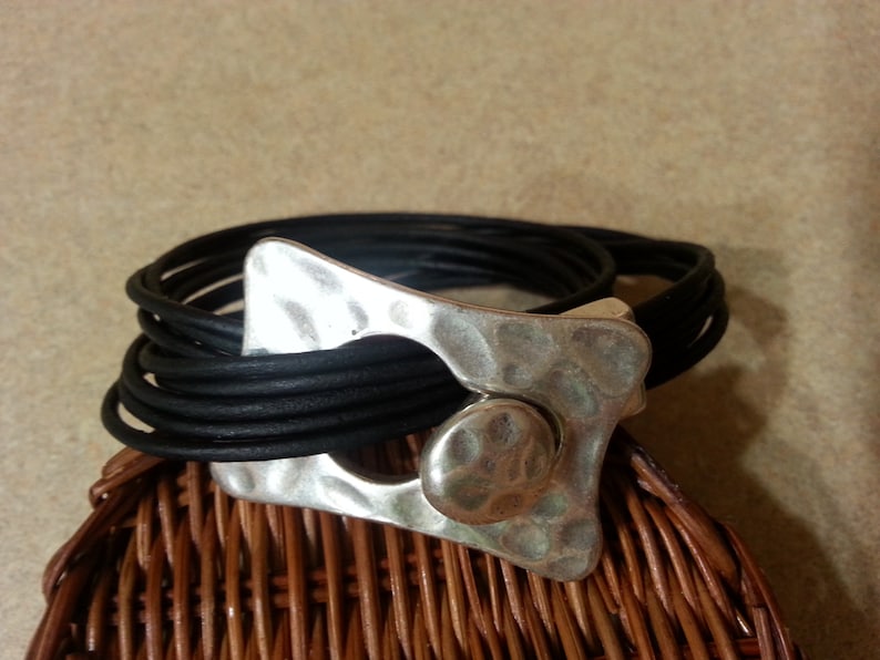 May include: A black leather wrap bracelet with a hammered silver clasp. The clasp has a large, round, hammered silver accent.