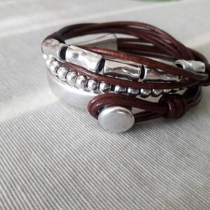 May include: A brown leather bracelet with silver beads and metal accents. The bracelet is wrapped around itself multiple times and has a silver clasp.
