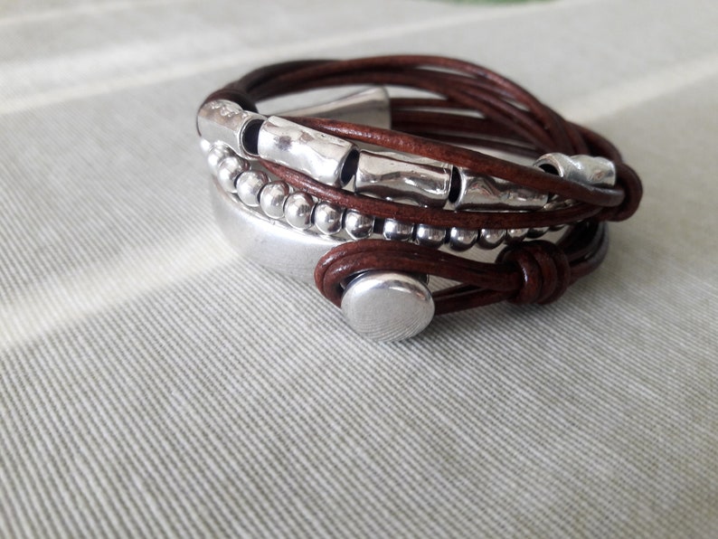May include: A brown leather bracelet with silver beads and metal accents. The bracelet is wrapped around itself multiple times and has a silver clasp.
