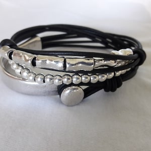 May include: A black leather bracelet with silver beads and a silver charm. The bracelet is layered with multiple strands of leather.