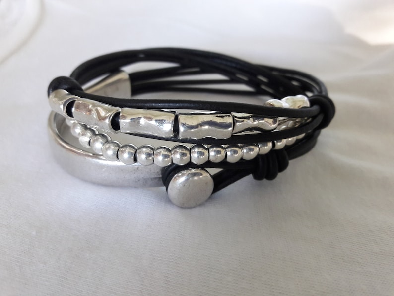 May include: A black leather bracelet with silver beads and a silver charm. The bracelet is layered with multiple strands of leather.