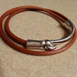 May include: A brown leather bracelet with a silver clasp. The bracelet is wrapped twice around the wrist.