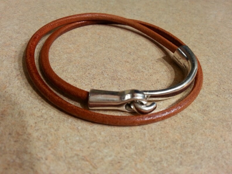 May include: A brown leather bracelet with a silver clasp. The bracelet is wrapped twice around the wrist.