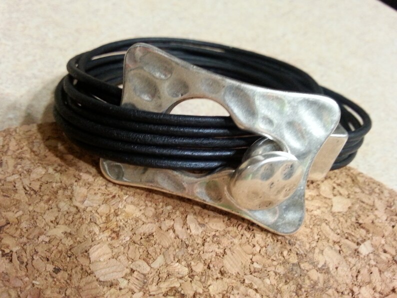 May include: A black leather bracelet with a silver, textured, abstract-shaped clasp.