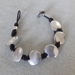 Puede incluir: Un brazalete de cuero negro con cuentas redondas plateadas. El brazalete tiene un cierre de bot&oacute;n.