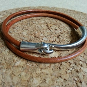 May include: A brown leather bracelet with a silver hook clasp. The bracelet is double-wrapped and has a smooth, polished finish.