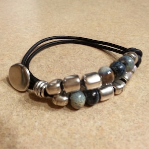 May include: A black leather bracelet with silver and blue beads. The bracelet has a silver clasp.