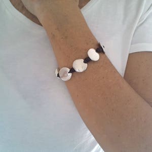 Puede incluir: Un brazalete de plata con abalorios redondos conectados por un cord&oacute;n marr&oacute;n.