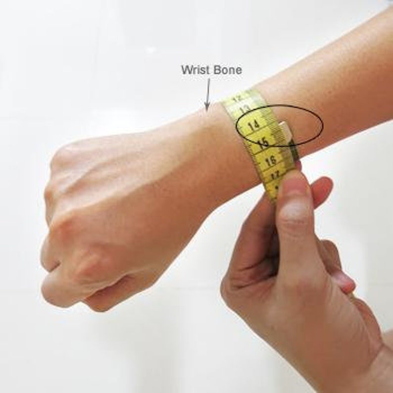 May include: A yellow measuring tape wrapped around a person's wrist to measure the wrist bone. The tape reads 12 to 17 inches.