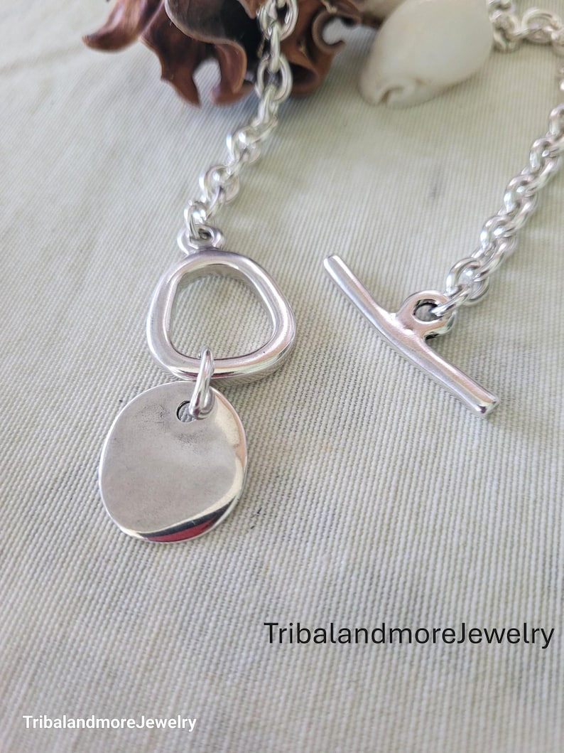 May include: A silver-toned bracelet with a toggle clasp. The bracelet features a chain link design, a circular pendant, and a unique asymmetrical ring. The text "TribalandmoreJewelry" is visible.