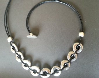 May include: A black leather necklace with silver oval-shaped beads. The necklace has a sliding clasp.
