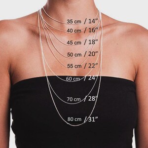 May include: A person wearing a black strapless top, showcasing a selection of silver chain necklaces. The necklaces vary in length, with measurements from 14 inches to 31 inches, and corresponding metric measurements in centimeters are also displayed.