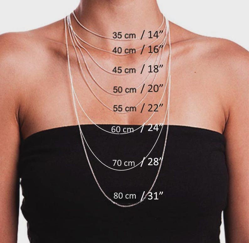 May include: A person wearing a black strapless top, showcasing a selection of silver chain necklaces. The necklaces vary in length, with measurements from 14 inches to 31 inches, and corresponding metric measurements in centimeters are also displayed.