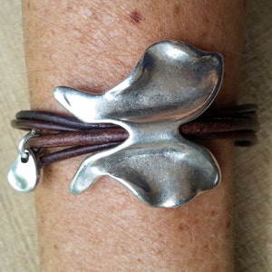 May include: A brown leather bracelet with a silver butterfly charm and a small silver teardrop charm.