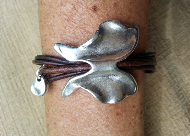 May include: A brown leather bracelet with a silver butterfly charm and a small silver teardrop charm.
