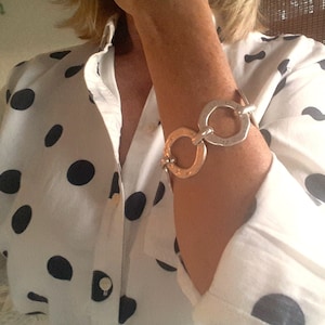 May include: A white shirt with black polka dots and a silver chain bracelet with multiple linked circles.