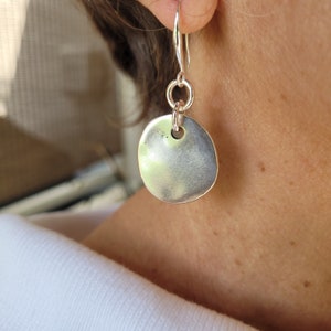 May include: Silver dangle earrings with a round disc pendant. The disc has a small hole in the center.