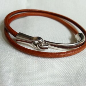 May include: A brown leather bracelet with a silver clasp. The bracelet is double-wrapped and has a simple design.