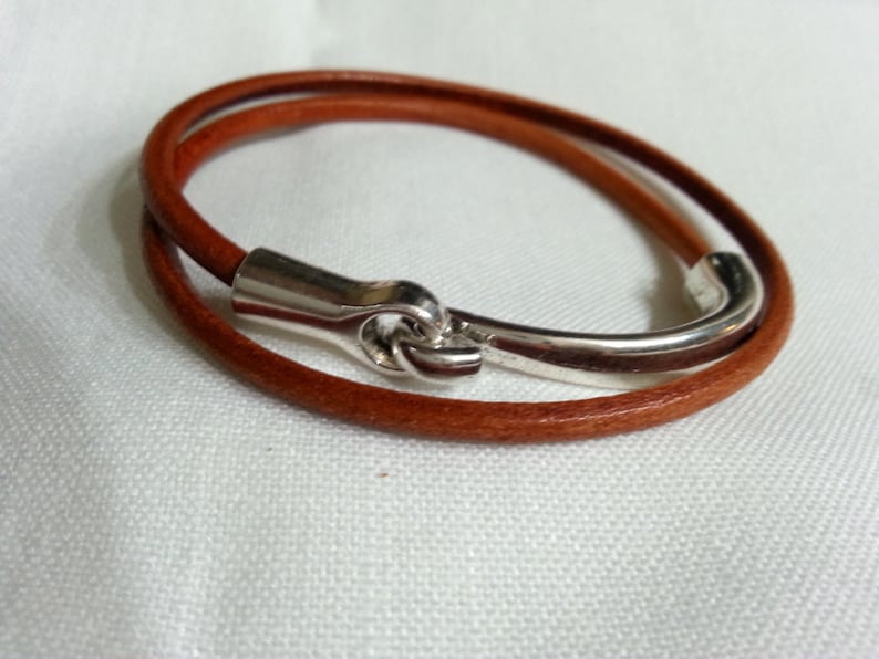 May include: A brown leather bracelet with a silver clasp. The bracelet is double-wrapped and has a simple design.