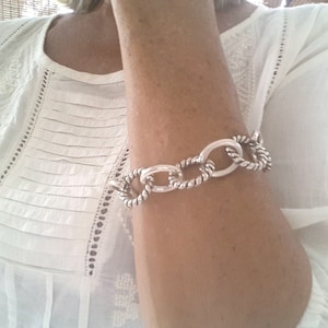 Op de afbeelding: Een zilveren kettingarmband met ovale schakels. De armband is gemaakt van gedraaid metaal en heeft een gepolijste afwerking.