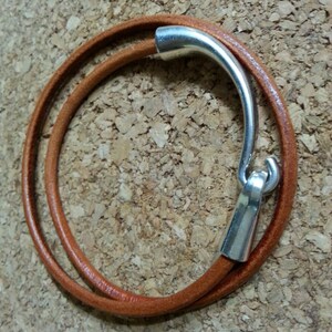May include: A brown leather bracelet with a silver clasp. The bracelet is double-wrapped and has a simple design.