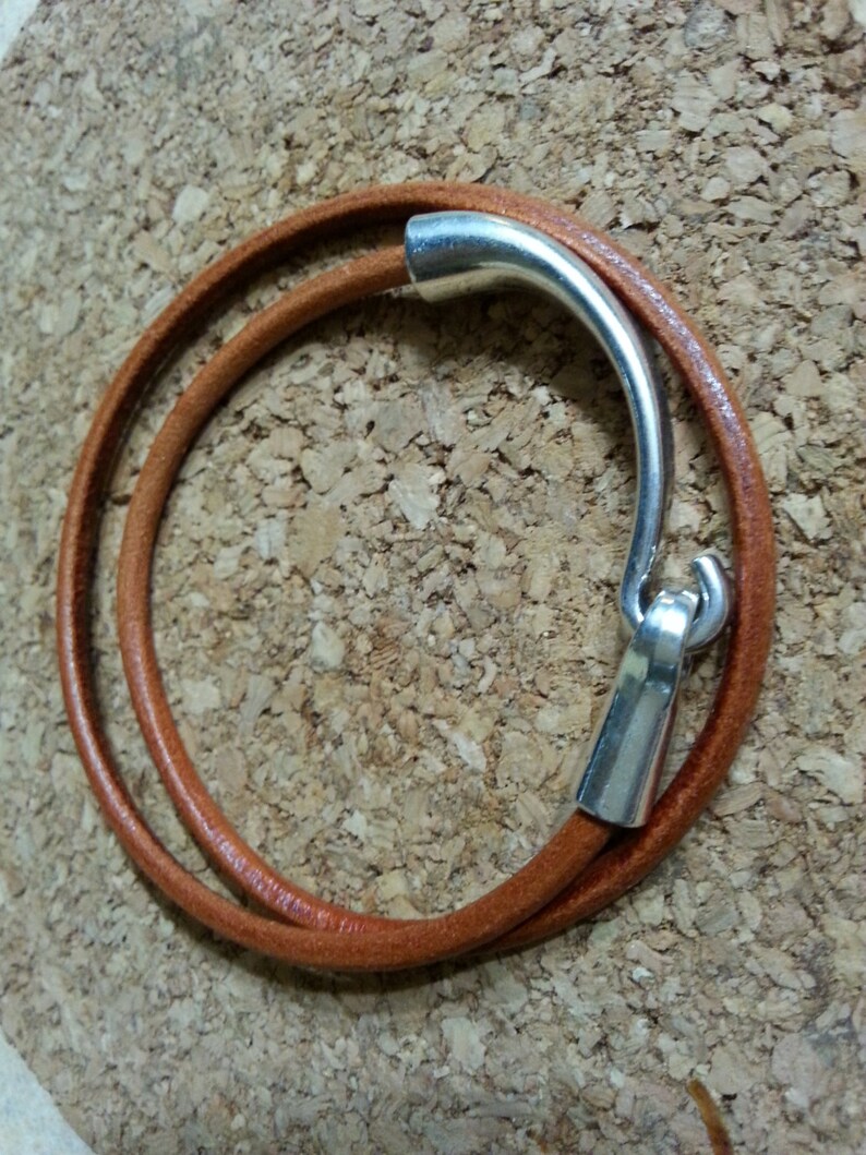 May include: A brown leather bracelet with a silver clasp. The bracelet is double-wrapped and has a simple design.