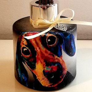 May include: A black diffuser bottle with a silver lid and a colourful dachshund illustration. The bottle has a yellow ribbon tied around it with a silver heart charm.