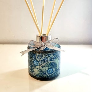 May include: A blue and green floral patterned diffuser bottle with a silver lid and a silver bow.  The bottle has wooden sticks inserted into the lid.