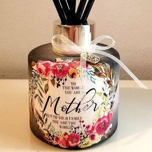 May include: A black glass diffuser bottle with a floral design and the text "To the world you are a Mother, but to your family you are the world". The bottle has a silver lid and a white ribbon with a silver charm. Black diffuser sticks are in the bottle.