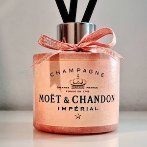 May include: A pink glass diffuser bottle with a silver lid and a pink ribbon bow. The bottle has a label that says "Champagne Epernay France Fondé en 1743 Moët & Chandon Impérial".