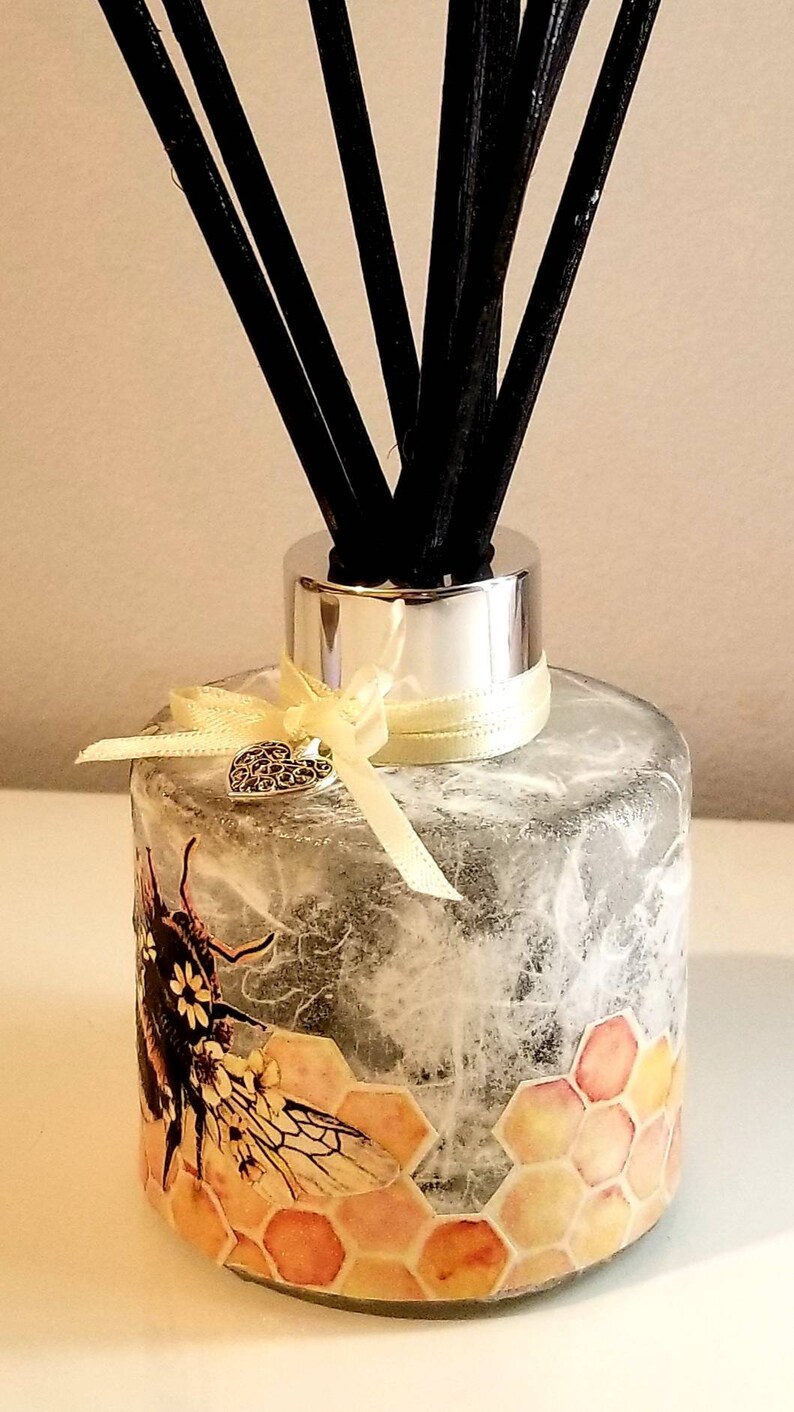 Peut inclure: Une bouteille diffuseur en verre transparent avec un couvercle argent&eacute; et des b&acirc;tonnets diffuseurs noirs. La bouteille est d&eacute;cor&eacute;e d'un motif en nid d'abeille et d'une illustration d'abeille. Un ruban jaune avec un charme de c&oelig;ur argent&eacute; est nou&eacute; autour du cou de la bouteille.