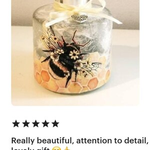 Peut inclure: Une bouteille en verre transparent avec un couvercle argent&eacute; et un ruban jaune. La bouteille est d&eacute;cor&eacute;e d'un motif d'abeille et de nid d'abeille avec des fleurs. La bouteille est un objet d&eacute;coratif.