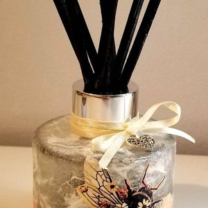Peut inclure: Une bouteille de diffuseur en verre transparent avec un couvercle argent&eacute; et des b&acirc;tonnets diffuseurs noirs. La bouteille est d&eacute;cor&eacute;e d'un motif en nid d'abeille et d'une abeille bourdon avec des fleurs. Un ruban jaune avec un charme de c&oelig;ur argent&eacute; est attach&eacute; autour de la bouteille.