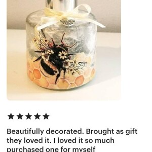 Peut inclure: Une bouteille diffuseur en verre transparent avec un couvercle argent&eacute; et un motif d'abeille d&eacute;coratif. L'abeille est entour&eacute;e de nids d'abeilles et de fleurs. La bouteille est attach&eacute;e avec un ruban blanc et un charme de c&oelig;ur argent&eacute;.