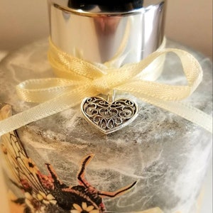 Peut inclure: Une bouteille de diffuseur en verre avec un motif d'abeille gris et orange. La bouteille a un couvercle argent&eacute; et un ruban jaune avec un charme de c&oelig;ur argent&eacute;.